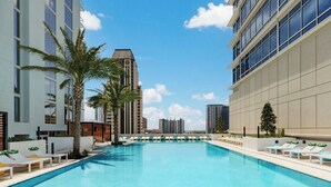 Una piscina con sillones de descanso y palmeras, rodeada de edificios modernos.