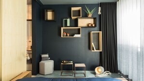 Un dormitorio moderno con una pared oscura, estanterías de madera, una cama, una mesita pequeña y una planta.