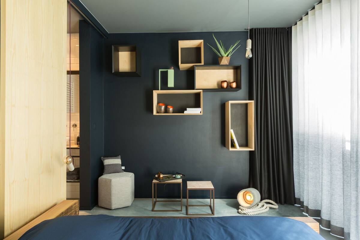 Une chambre à coucher moderne avec un mur foncé, des étagères en bois, un lit, une petite table et une plante.