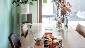 Un comedor con una mesa de madera, varios botes de conservas, una planta en maceta y una lámpara colgante.