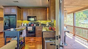 A modern kitchen with wooden cabinets, a stainless steel refrigerator, a microwave, and a stove. There is a wooden deck outside with a railing.