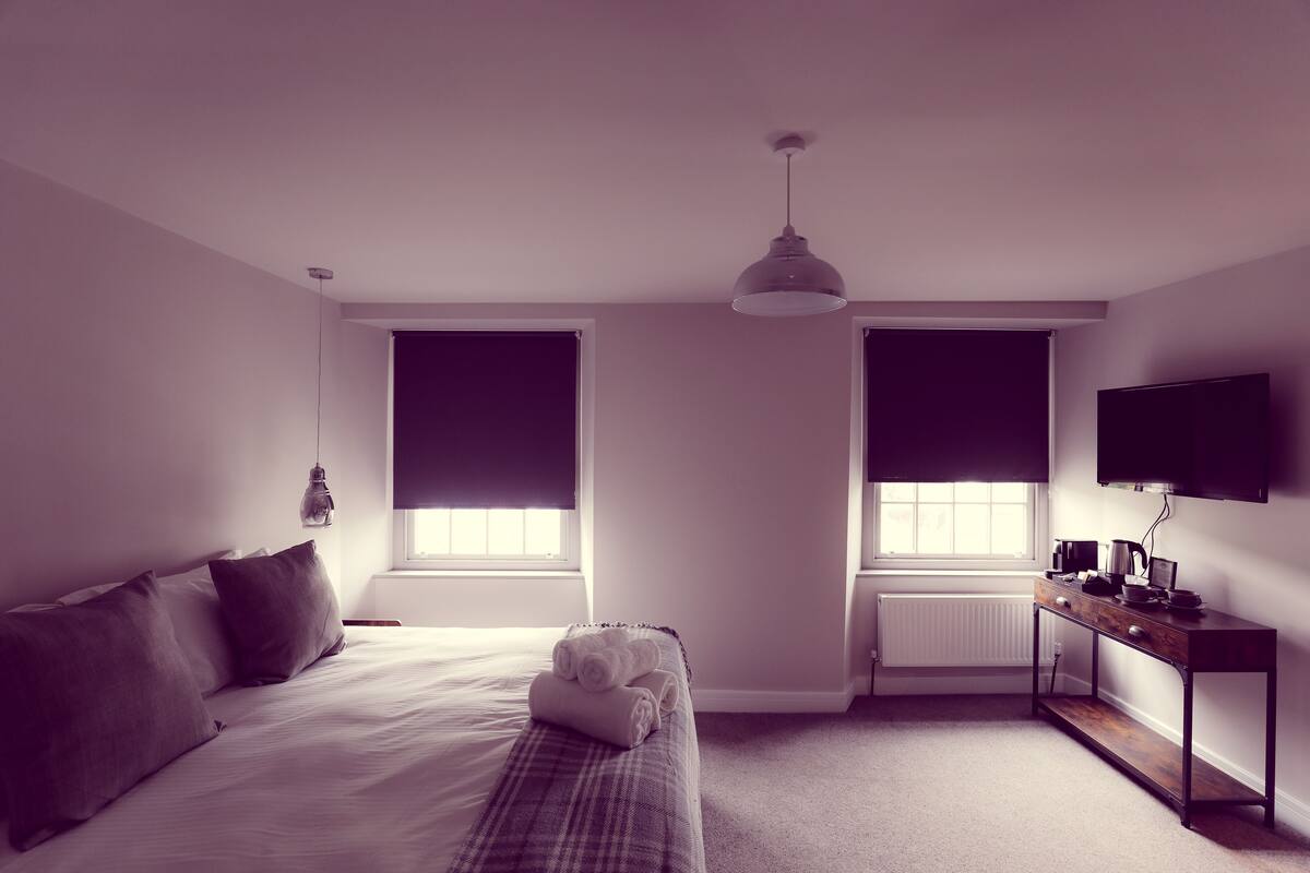 A bedroom with a bed, a bedside table, a desk, and a TV.