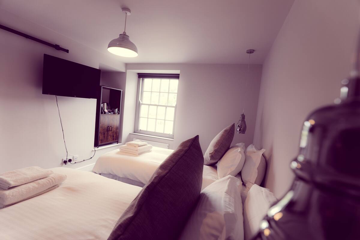 A modern hotel room with a large window, a flat-screen TV mounted on the wall, and a neatly made bed with pillows and a folded towel.