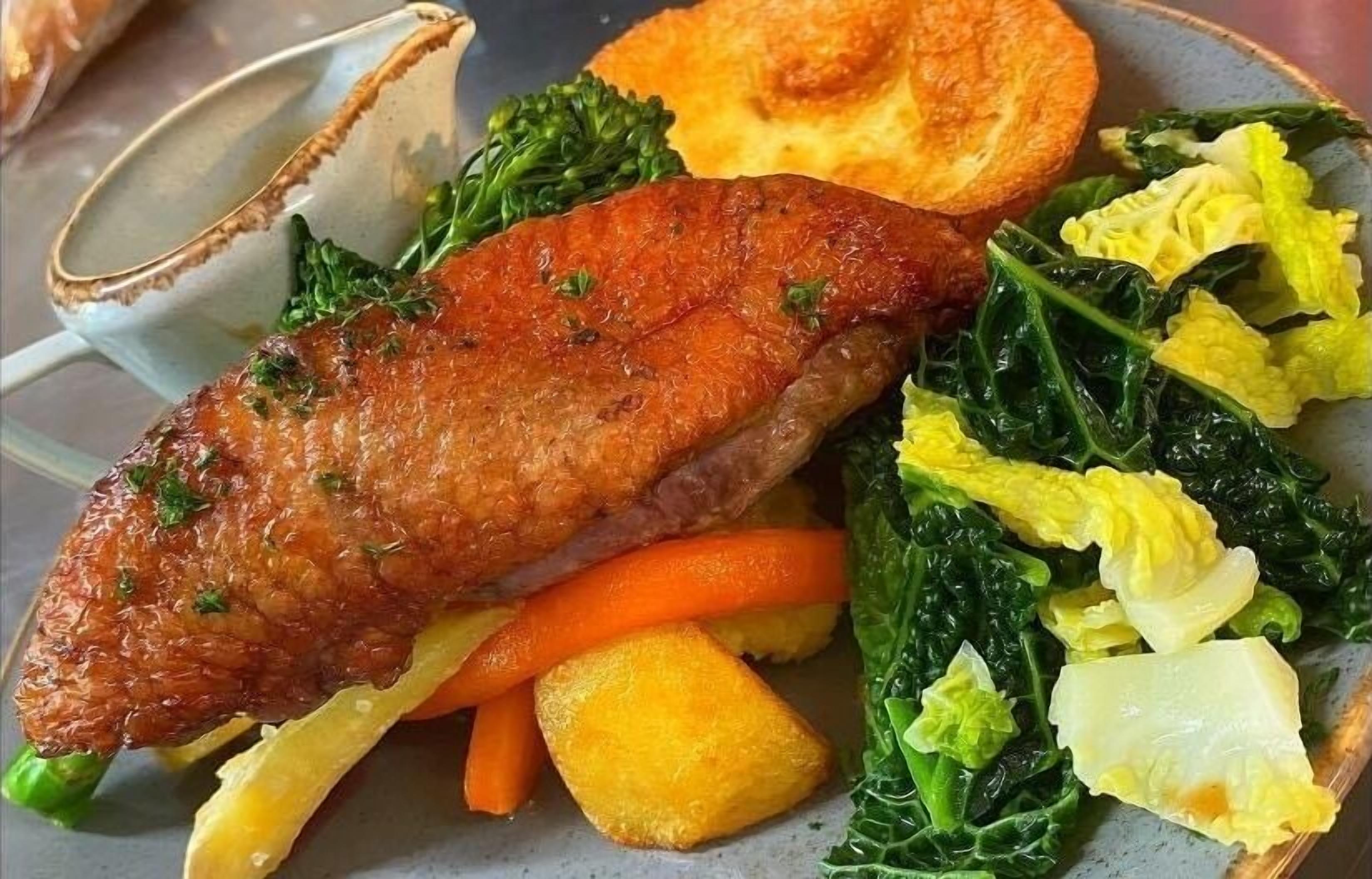 A plate with roasted duck, vegetables, and a side of bread.