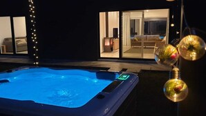 Ein Whirlpool mit Bedienfeld, eine Glastür zu einem Wohnzimmer mit Sofa und Fernseher sowie Lichterketten.