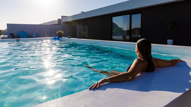 Ein moderner Poolbereich mit klarem Wasser, eine Person entspannt am Pool und ein zeitgenössisches Gebäude im Hintergrund.