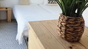 Ein Schlafzimmer mit einem Bett, einem Nachttisch, einer Lampe und einem Blumentopf auf einer Holzkommode.