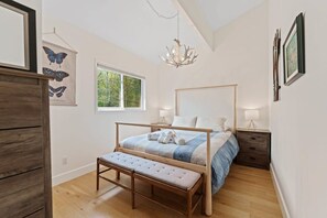 A bedroom with a wooden bed, a bench, a chandelier, and a window with a view of trees.