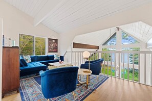A room with a blue sofa, a round table, and a view of the outdoors through large windows.