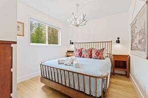 A bedroom with a bed, a window, a chandelier, and a nightstand. - Muskokan Mirage Located on Mirage Lake (Novar)