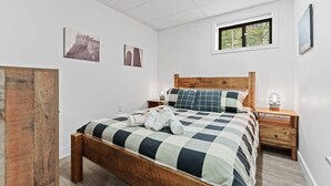 Makuuhuoneessa on puinen sänky, yöpöytä, ikkuna ja seinälle kiinnitetty taideteos.
