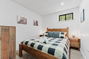 A bedroom with a wooden bed, a nightstand, a window, and wall-mounted artwork. - Muskokan Mirage  Located on Mirage Lake (Novar)