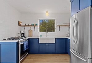 A modern kitchen with blue cabinets, a stainless steel refrigerator, and a window above the sink. - Muskokan Mirage Located on Mirage Lake (Novar)