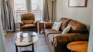 A living room with a brown leather sofa, a glass coffee table, a wooden side table, and a floor lamp.