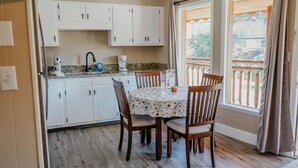 A kitchen with white cabinets, a dining table with chairs, and a view of a balcony through a window.