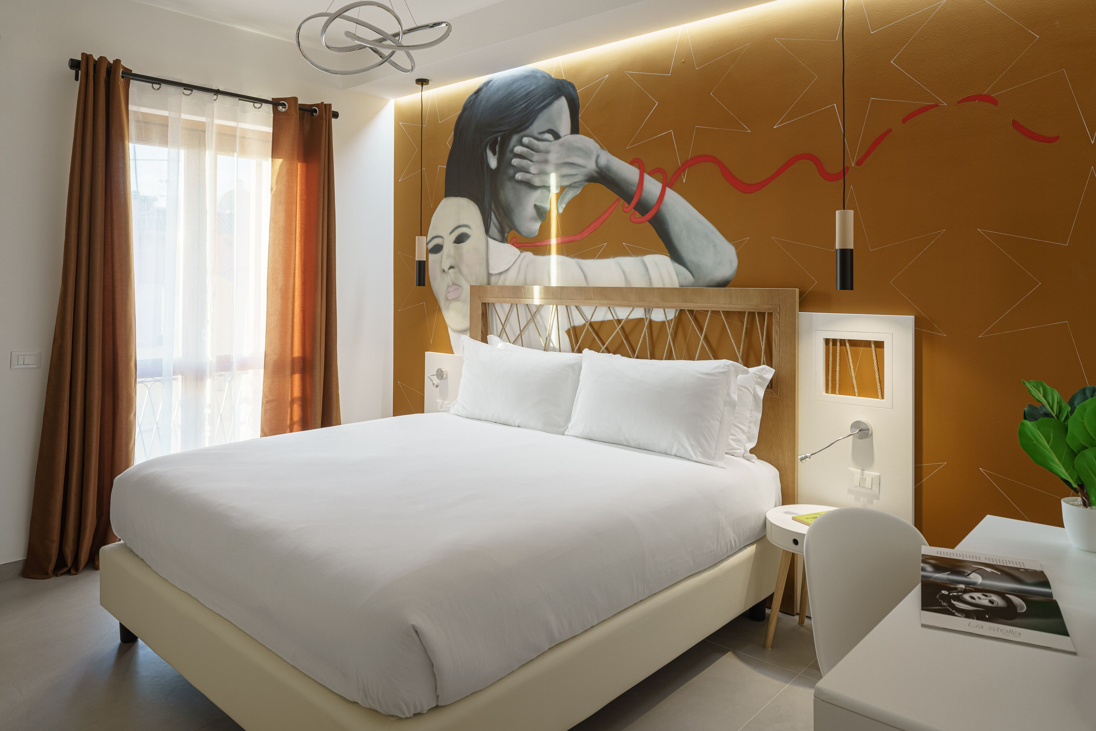 A modern hotel room with a large bed, a small bedside table, a chair, and a wall mural.