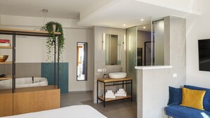 A modern bathroom with a freestanding bathtub, a large mirror, a sink on a wooden vanity, and a blue sofa with yellow cushions. - Urban Karalis by Accomodo (Cagliari)