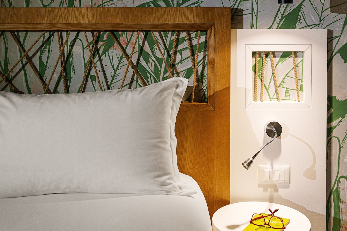Un dormitorio con una cama, una mesita de noche con lámpara y una pared decorada con un diseño de hojas verdes.
