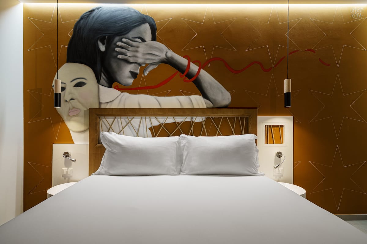 Una habitación de hotel moderna con una cama grande, un cabecero de diseño geométrico y un mural en la pared.