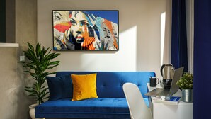 A modern living room with a blue sofa, a white desk, and a large abstract painting on the wall. - Urban Karalis by Accomodo (Cagliari)