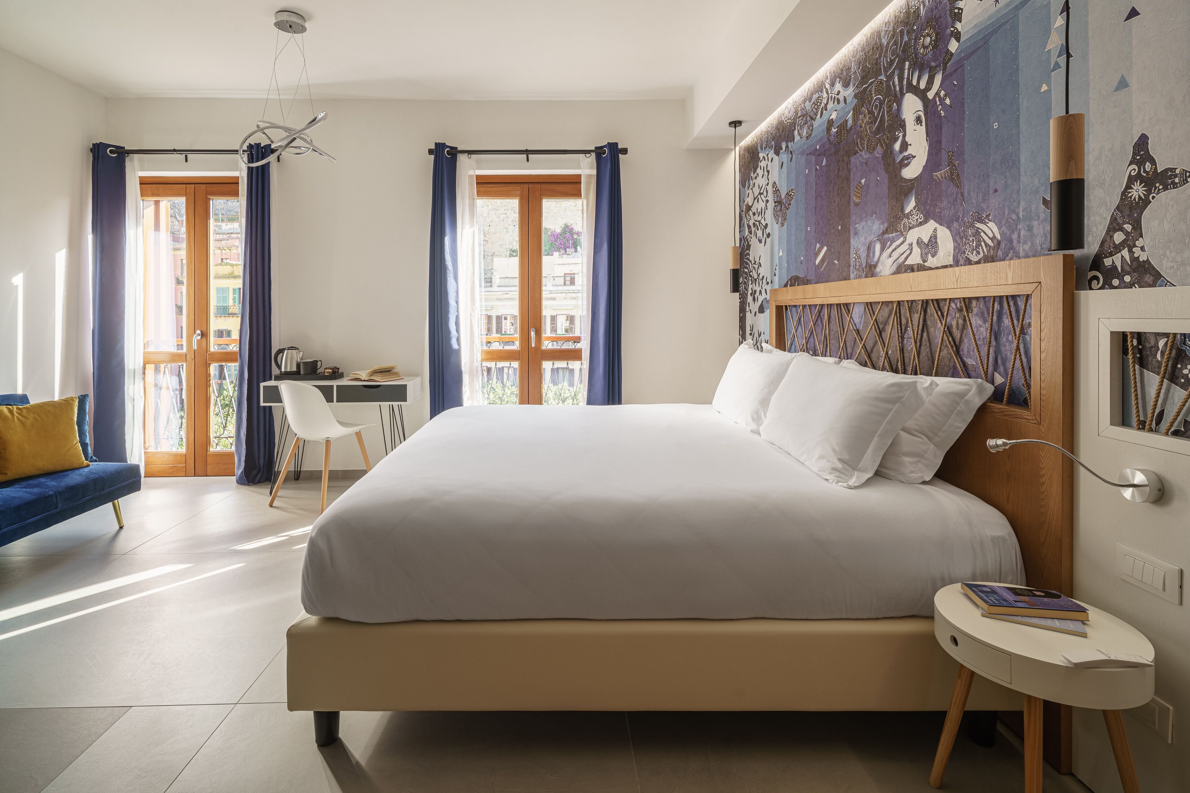 A modern bedroom with a large bed, a desk, and a chair. There is a view of the outside through a glass door.