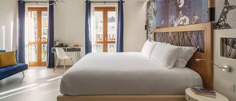 Un dormitorio moderno con una cama grande, un escritorio y una silla. Se ve el exterior a través de un ventanal.