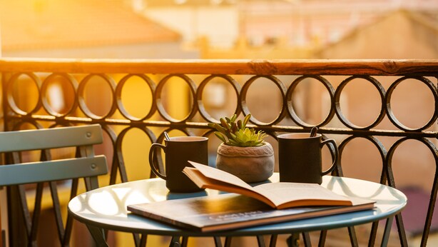 A table with a book, two mugs, and a small plant on a balcony with a metal railing. - Urban Karalis by Accomodo (Cagliari)