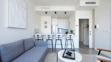 Una sala de estar moderna con un sofá gris, una mesa de centro y una cocina al fondo.