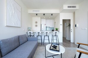 A modern living room with a grey sofa, a coffee table, and a kitchen in the background. - The First Suite Apartment (Granada)