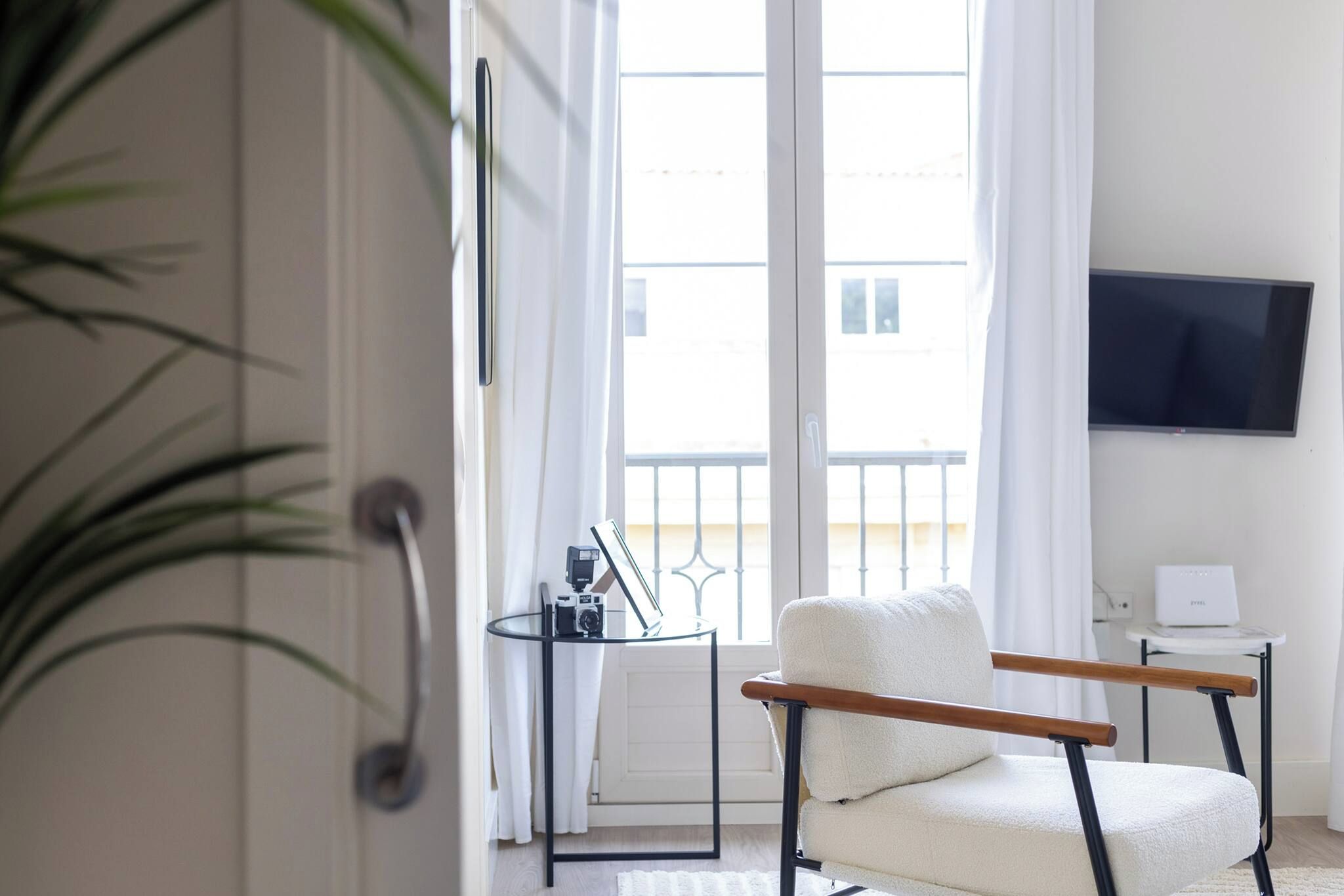A modern living room with a sofa, a television, and a balcony view.