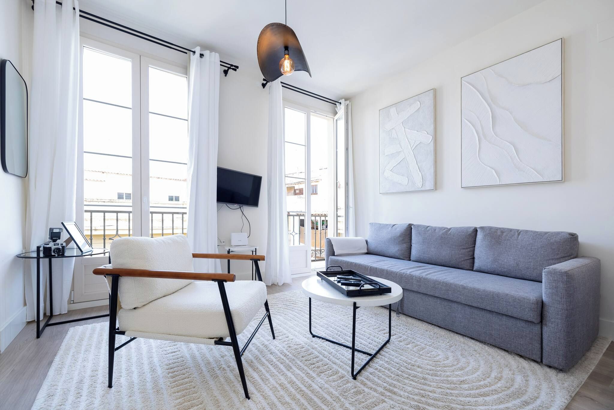 Un salon moderne avec un canapé gris, un fauteuil blanc, une table basse ronde et un téléviseur à écran plat fixé au mur.