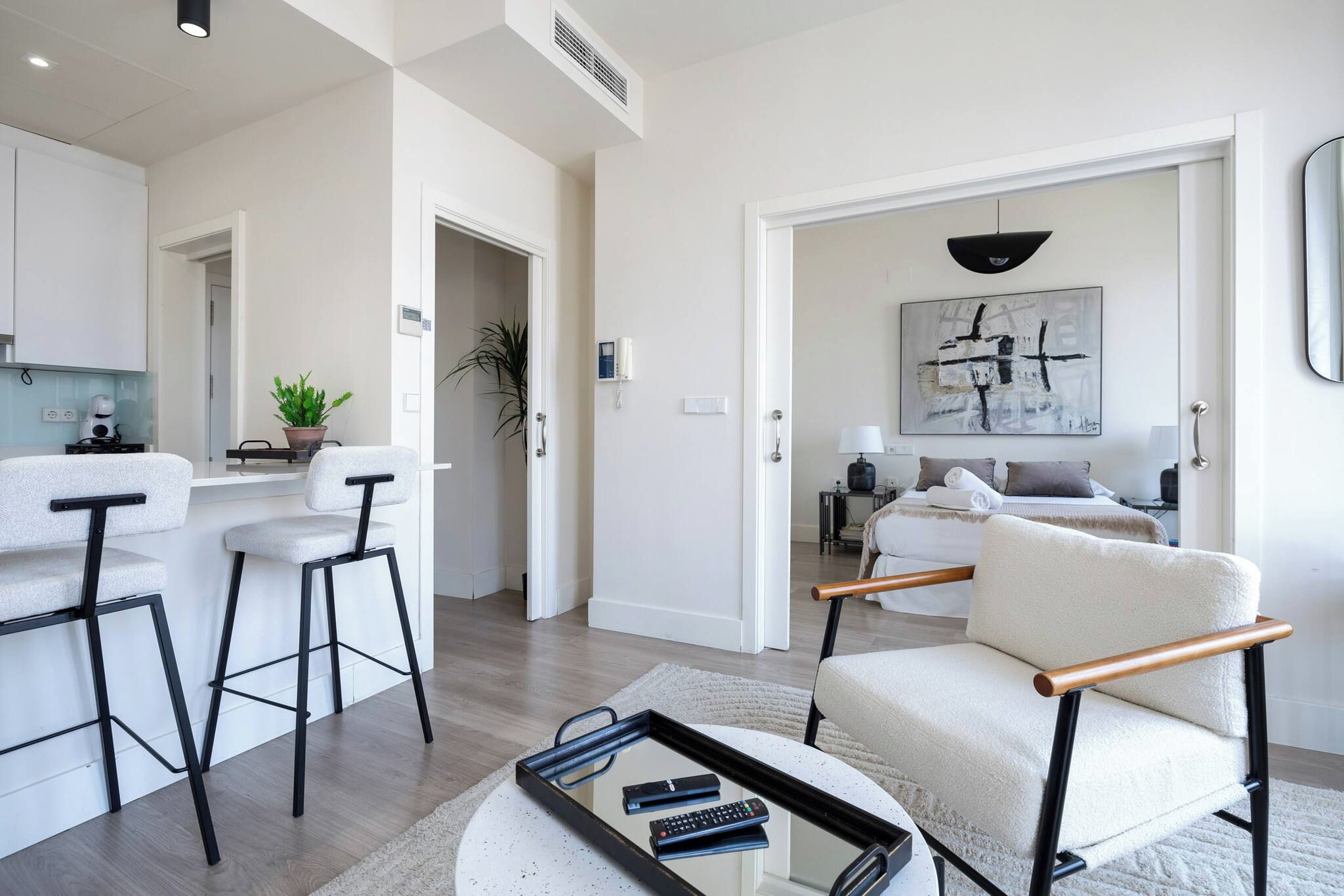 Una sala de estar moderna con un sofá, una mesa de centro y un televisor. Hay una zona de cocina con refrigerador, estufa y lavaplatos. La habitación tiene un ventanal y una puerta que conduce a otra estancia.