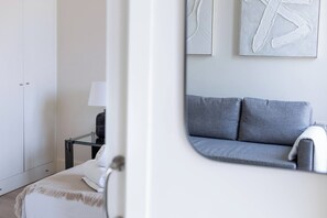 A modern bedroom with a grey sofa, a bedside table with a lamp, and a wardrobe. - The First Suite Apartment (Granada)