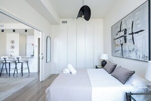 A modern bedroom with a large bed, a desk, and a bathroom in the background. - The First Suite Apartment (Granada)