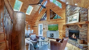 Interior de una cabaña de madera con chimenea, televisión y una zona de estar acogedora.