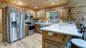 Una cocina de estilo cabaña de madera con un refrigerador de acero inoxidable, microondas, horno y pileta.