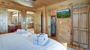 Ein Zimmer in einer Holzhütte mit einem Bett, einem Deckenventilator, einem Fernseher und Blick ins Freie.