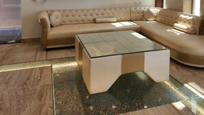 A modern living room with a beige sectional sofa, a glass coffee table, and a decorative wall panel.