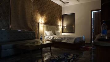 A modern hotel room with a bed, a sofa, a glass coffee table, and a large mirror.