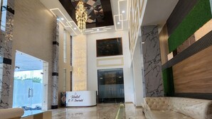 A modern hotel lobby with marble flooring, a chandelier, and a reception desk labeled "Hotel P. Emerald".