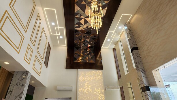 A spacious lobby with a high ceiling, geometric wall designs, a chandelier, and a plush sofa.
