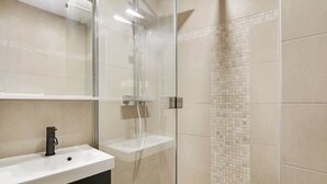 Ein modernes Badezimmer mit einer gläsernen Duschkabine, einem weißen Waschbecken und einer gefliesten Rückwand.