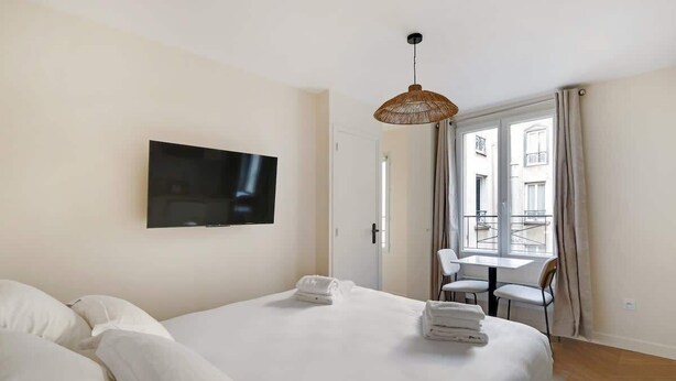 Ein Hotelzimmer mit Bett, Fernseher, Esstisch mit Stühlen und einem Balkon mit Vorhängen.