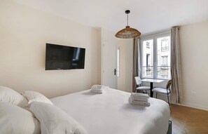 A hotel room with a bed, a TV, a dining table with chairs, and a balcony with curtains. - A cozy studio in Saint-Lazare (Paris)