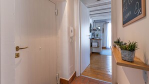A hallway with a white door, a wooden floor, and a kitchen area visible through an open door. There are potted plants on a shelf and a sign on the wall. - Sant'Onofrio Mini Loft by Wonderful Italy (Palermo)