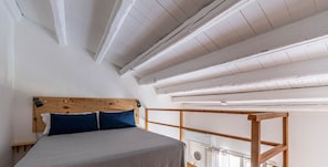 Une chambre à coucher avec un lit, une tête de lit en bois et un balcon doté d’une balustrade en bois.