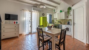 Ein Essbereich mit Tisch und Stühlen, ein Fernseher auf einer Kommode, ein grüner Kühlschrank und eine Küche im Hintergrund.