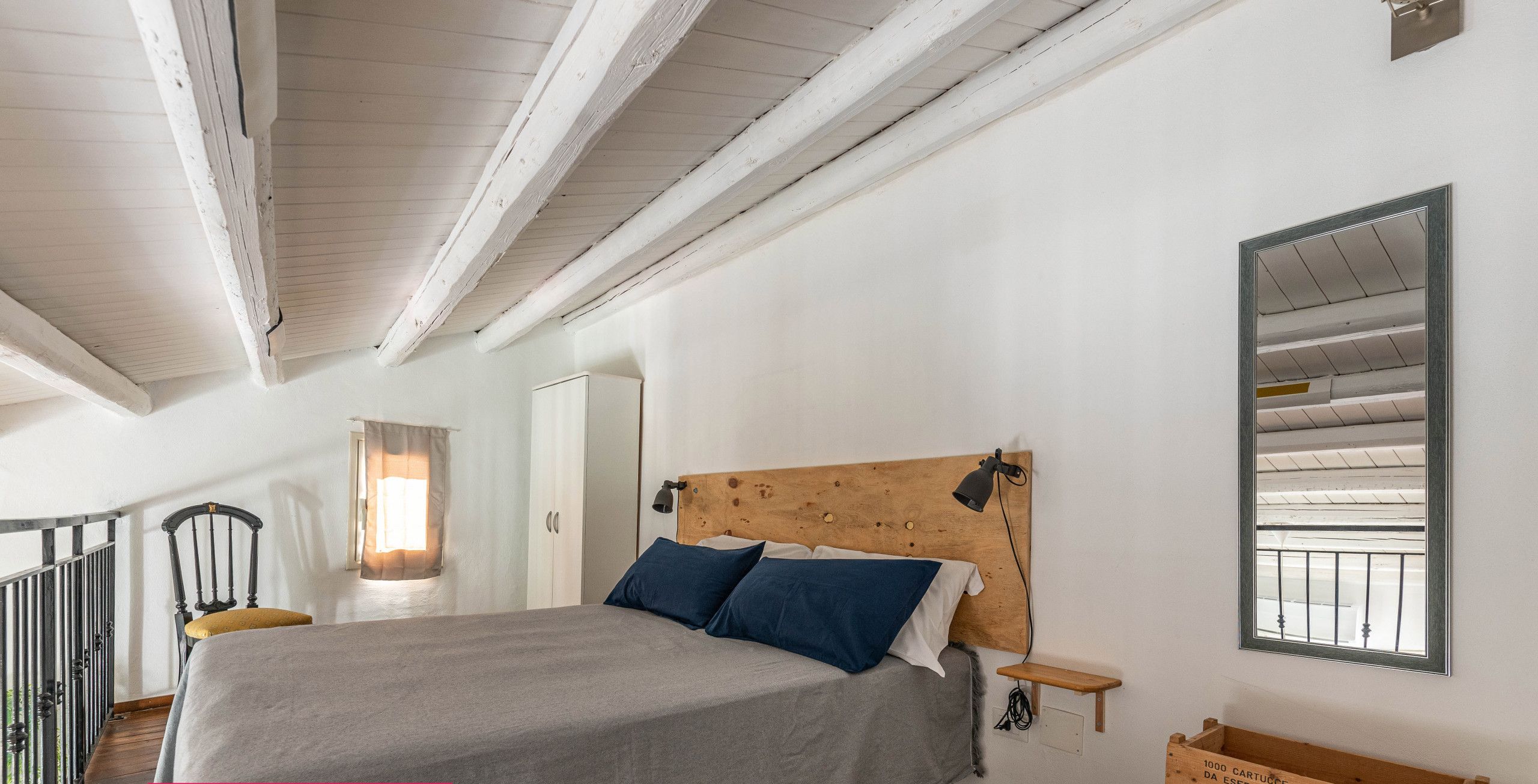 A bedroom with a bed, a nightstand, a wooden headboard, a mirror, and a small table.