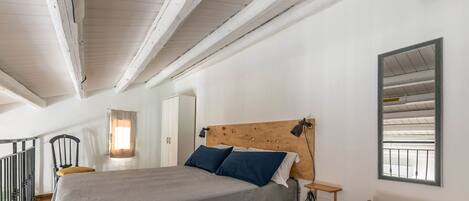 A bedroom with a bed, a nightstand, a wooden headboard, a mirror, and a small table.