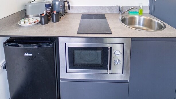 A compact kitchen with grey cabinets, a built-in oven, a microwave, a toaster, and a sink. - Spacious 1-bed Studio in Birmingham (Birmingham)